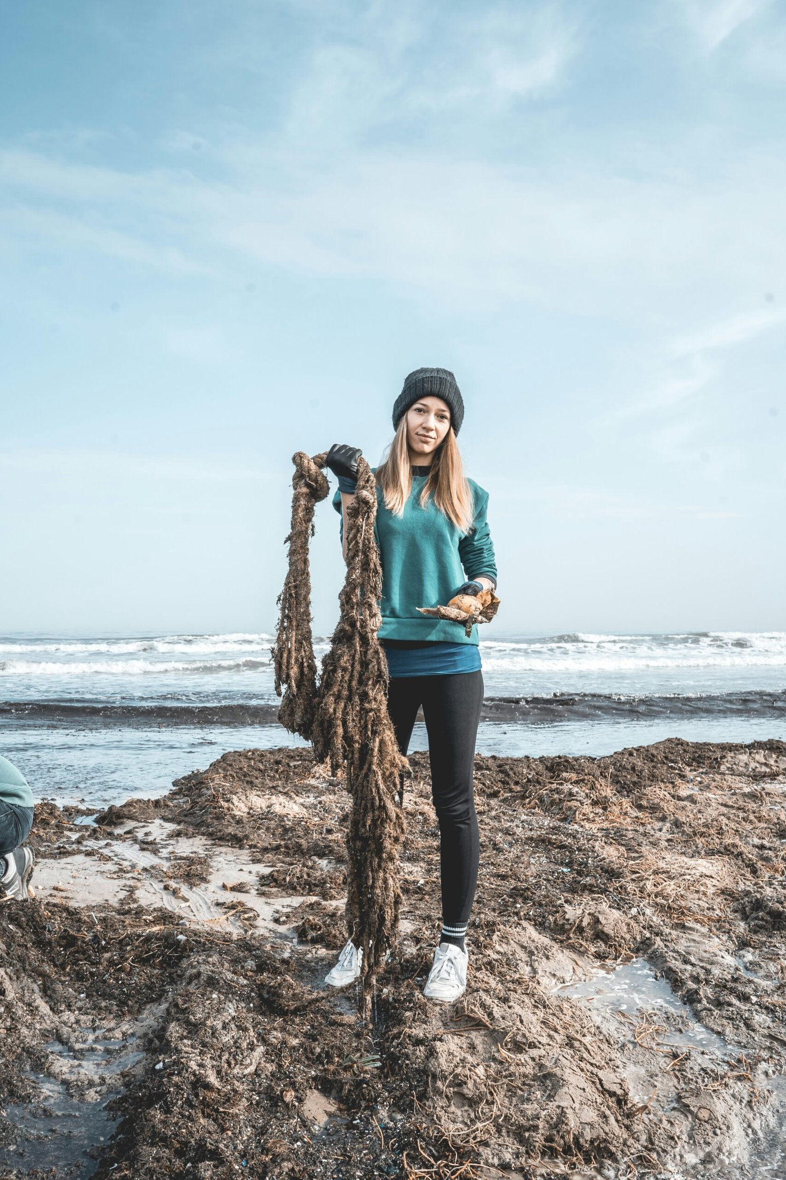 woman in teal long sleeve shirt and black pants standing on brown tree trunk near sea